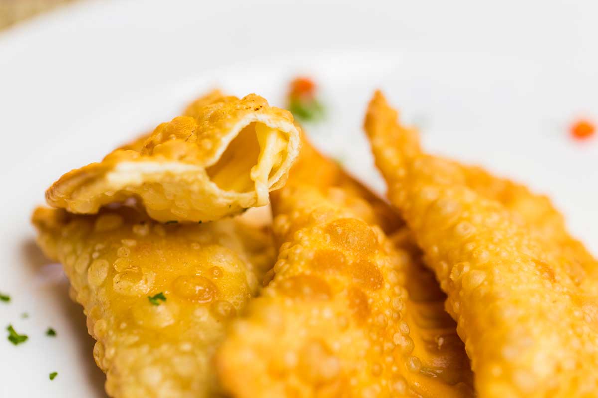 Nahaufnahme von goldbraun frittierten Pastechis auf einem weißen Teller – ein typischer arubanischer Streetfood-Snack, knusprig und cremig gefüllt.